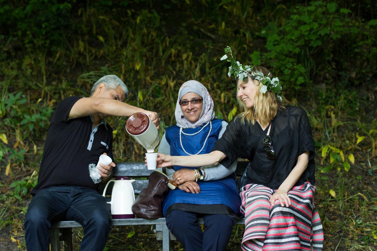 Smiling Henna wearing a white poplar garland and sharing coffee with two happy participants.