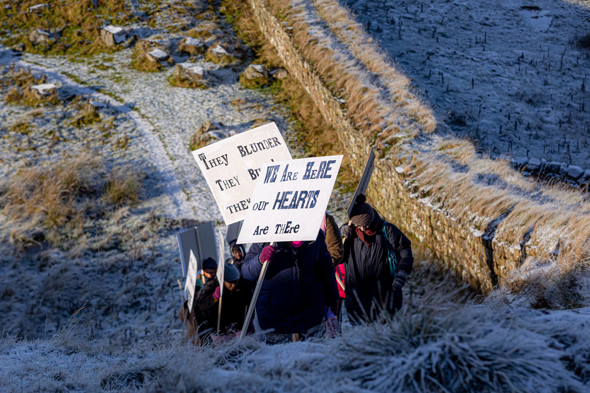 People holding banners and walking uphill by Hadrian’s Wall.