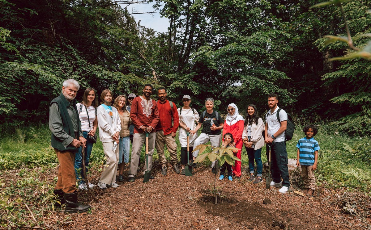 A group of people standing behind a newly planted tree.